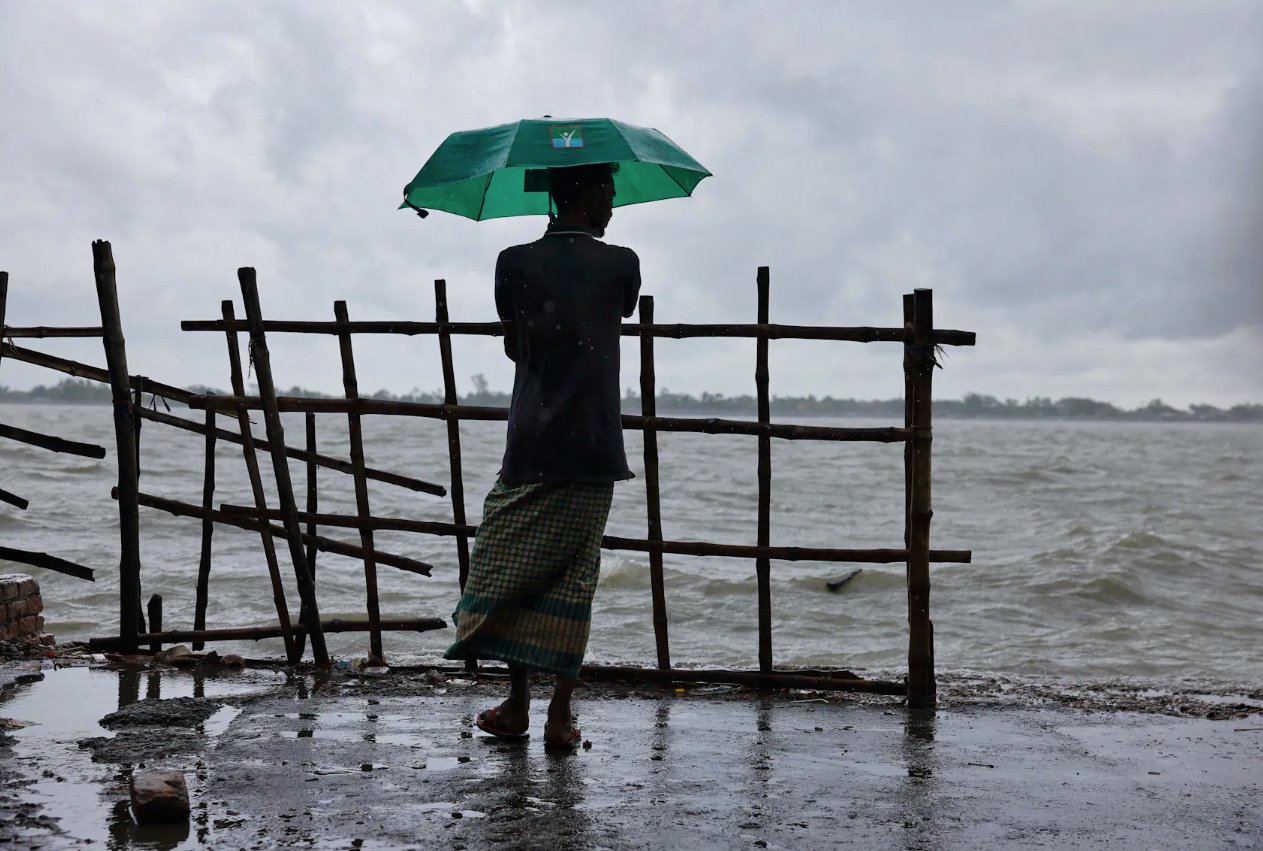2024年5月26日，在飓风“雷马尔”袭击孟加拉国萨特希拉Shyamnagar地区之前，一名男子撑着雨伞站在Kholpetua河岸上。